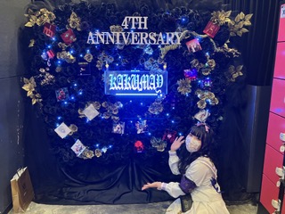 「4th Anniversary KAKIMAY」と書いてあるリースの前で手を広げてポーズを取る凜さんの写真