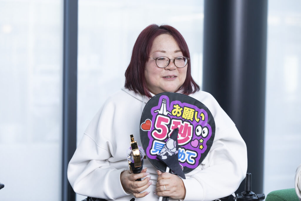 「お願い5秒見つめて」と書いてあるうちわを持っている弘美さんの写真
